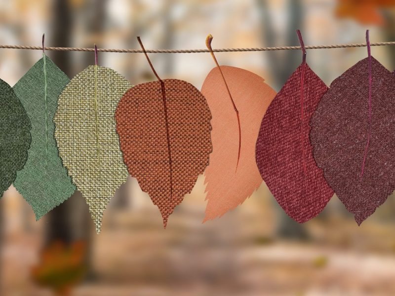 Fabric leaves in green, red, orange, and purple colors hanging from twine outdoors