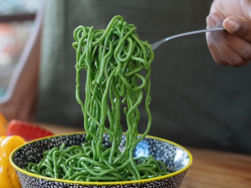 Person picking up green noodles with a fork