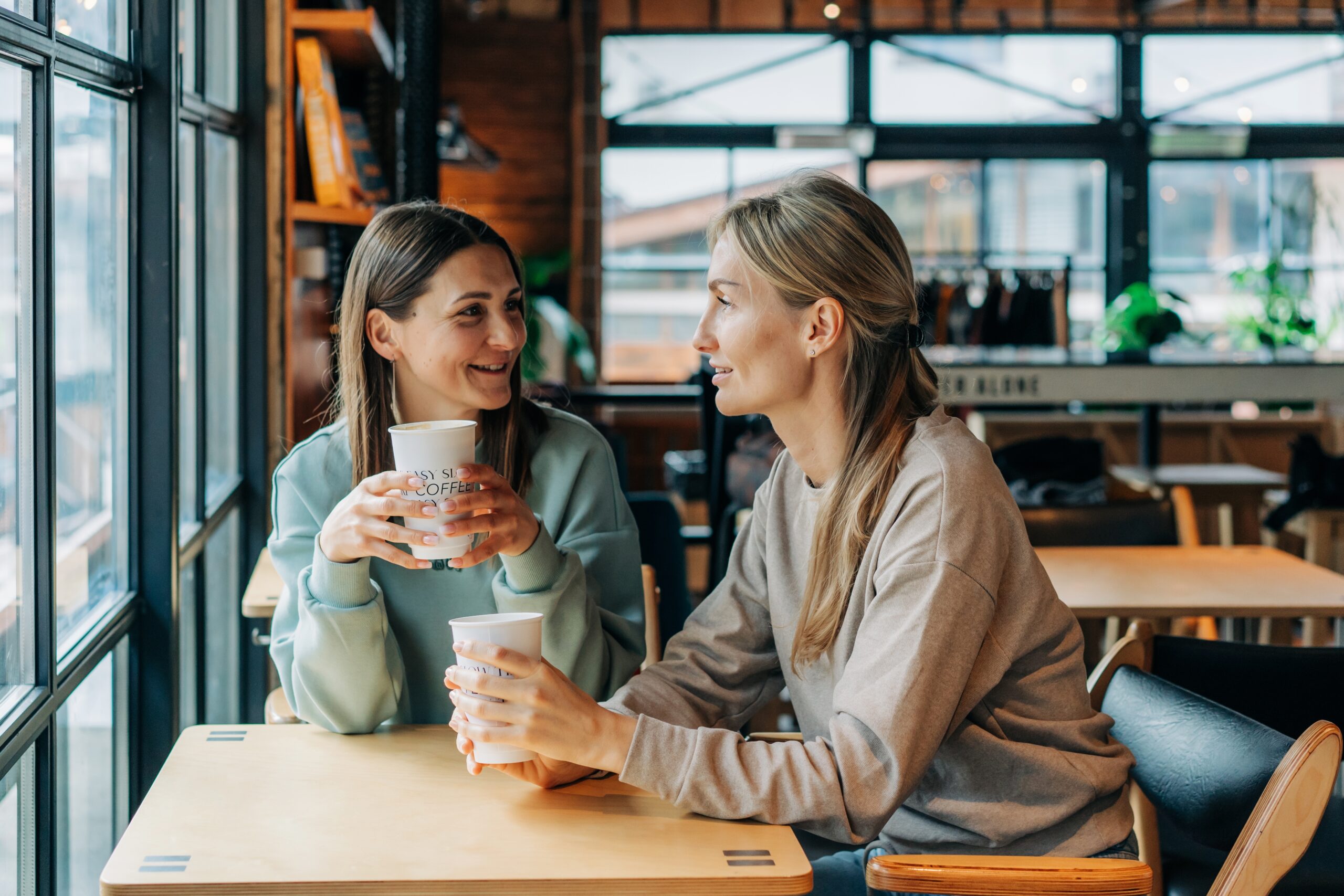 Two women chatting over questions to ask a potential roommate in a coffee shop sitting at a table.