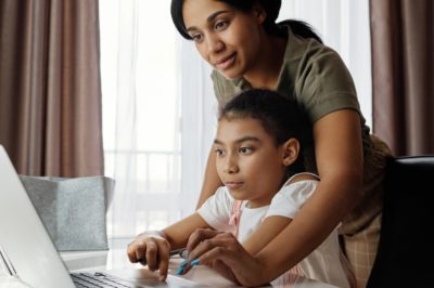 mother helping daughter on laptop