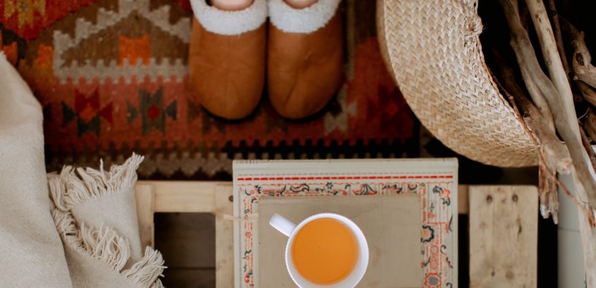 Person in house shoes standing on rug in front of small table with a cup of tea sitting on top of book.