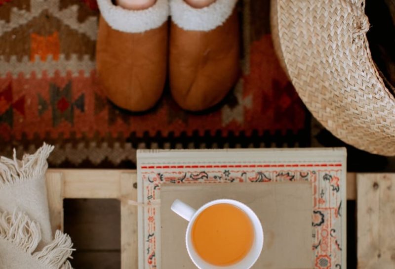Person in house shoes standing on rug in front of small table with a cup of tea sitting on top of book.