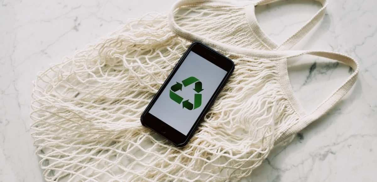 Phone with "reuse, reduce, recycle" logo on the screen laying on a fabric bag