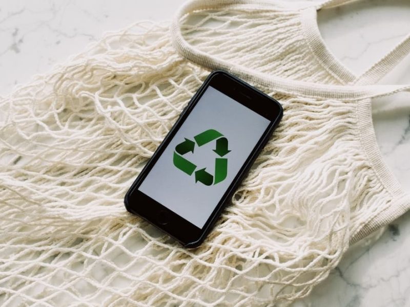 Phone with "reuse, reduce, recycle" logo on the screen laying on a fabric bag
