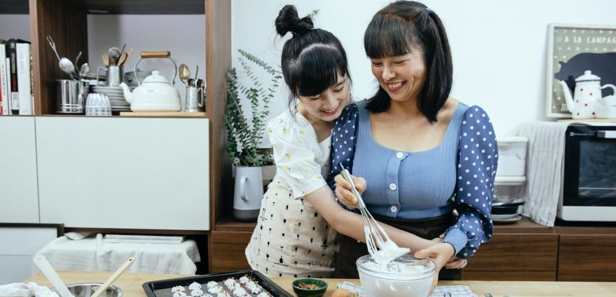 Smiling mother and daughter embracing while baking in kitchen