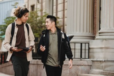 Two multi-racial young men walking and talking on college campus.