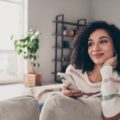 Woman sitting on couch with phone wondering if apartments come furnished in stylish loving room decorated by CORT Furniture Rental.
