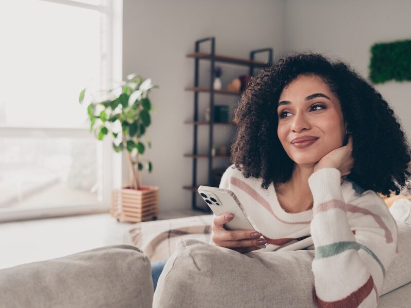 Woman sitting on couch with phone wondering if apartments come furnished in stylish loving room decorated by CORT Furniture Rental.