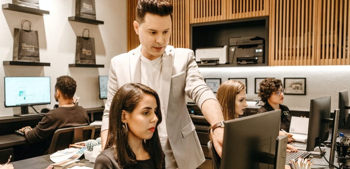 Man teaching woman in front of computer monitor in office.