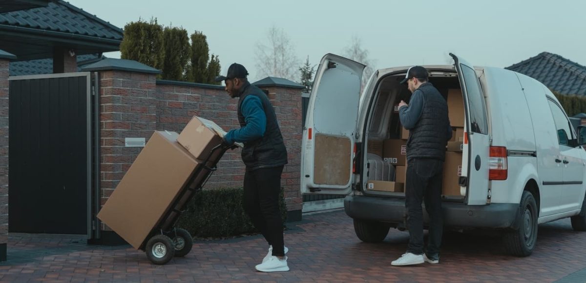 Two movers removing boxes from van and taking them into house on trolley.