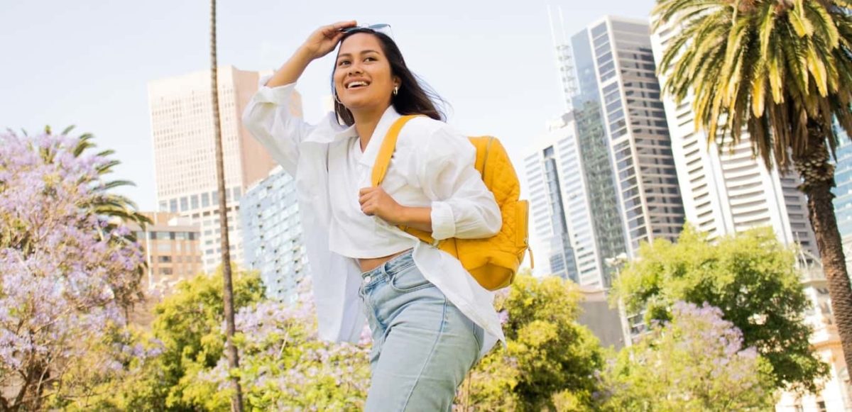 Woman in yellow backpack walking happily in city