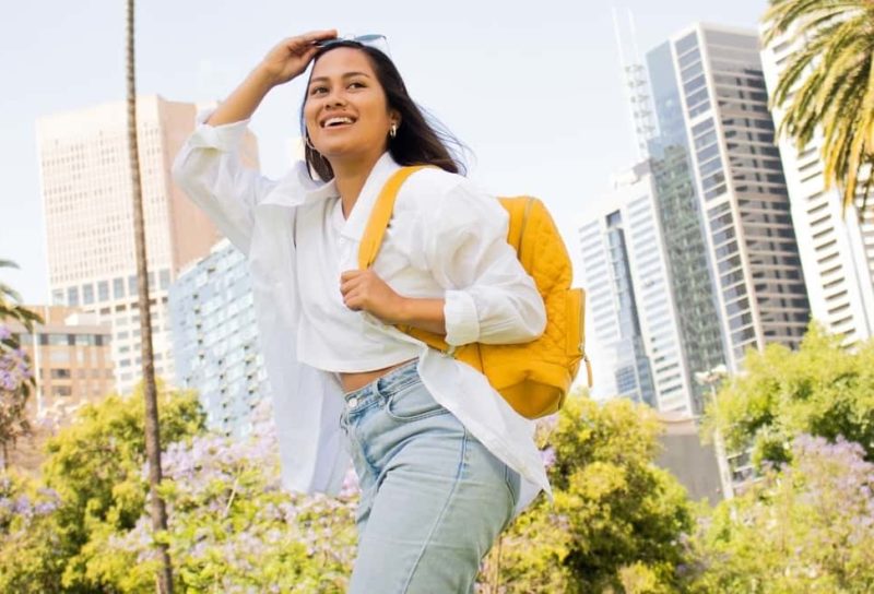 Woman in yellow backpack walking happily in city