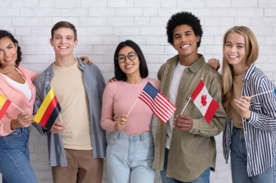 Diverse group of 5 teens smiling and holding flags from different countries.