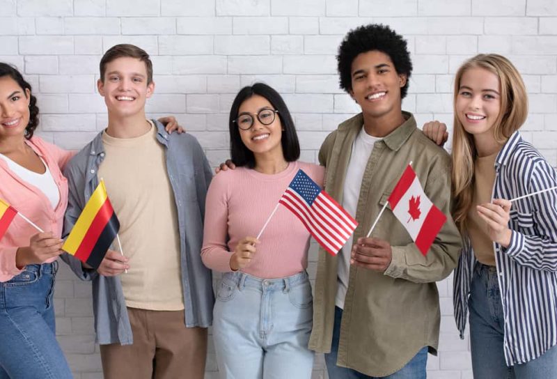 Diverse group of 5 teens smiling and holding flags from different countries.