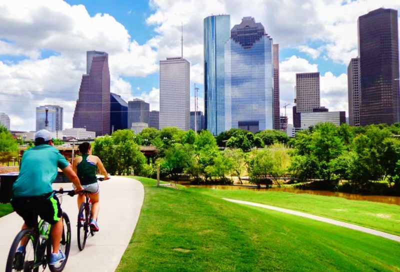 Man and woman riding bikes on a trail with Downtown Houston in the backdrop.