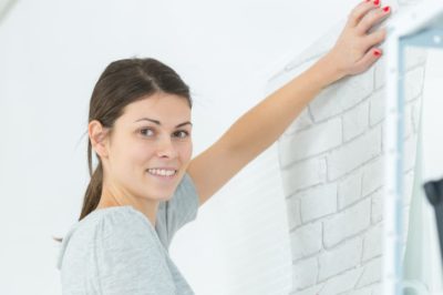 Woman installing wallpaper while smiling at the camera.