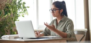 Woman in glasses sitting in front of computer with paper and pen in hand.