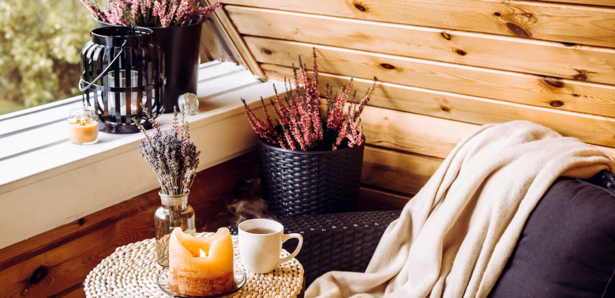 Fall hygge decor featuring candle, dried florals, a cozy blanket, and a hot cup of tea on a woven table