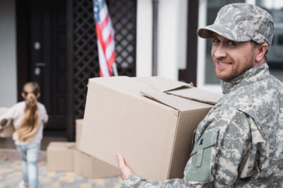 Smiling serviceman carries box to move into new home after military relocation.