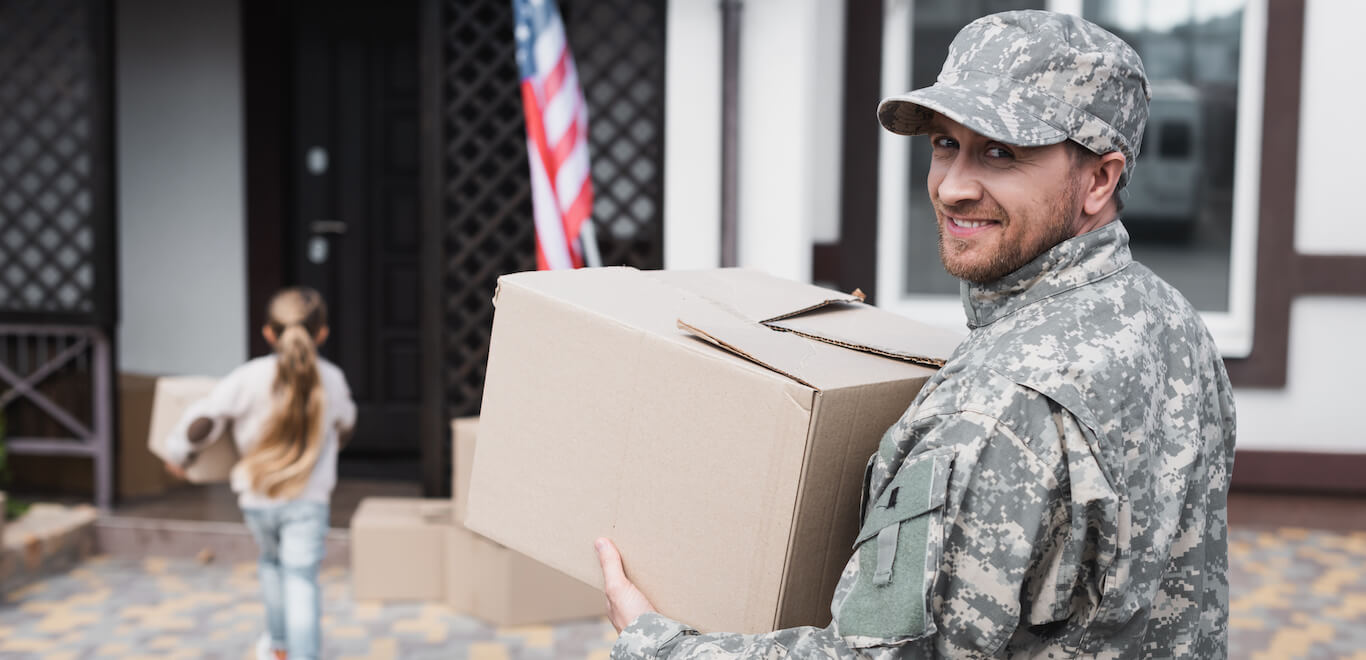 Smiling serviceman carries box to move into new home after military relocation.
