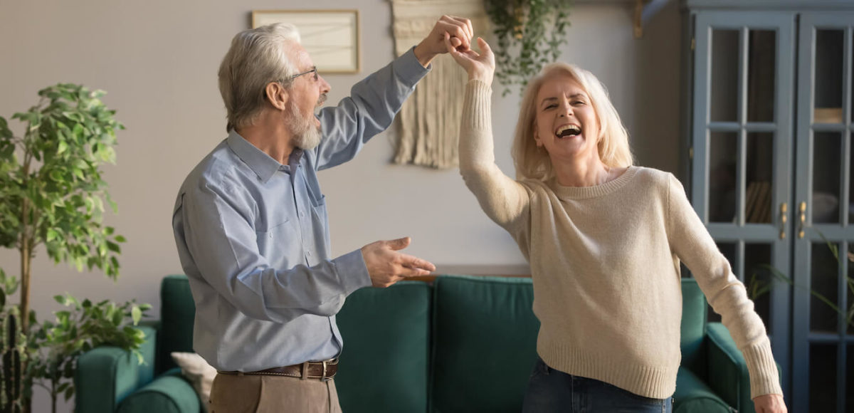 Senior couple is happy dancing in living room enjoying the freedom of renting after selling primary residence.