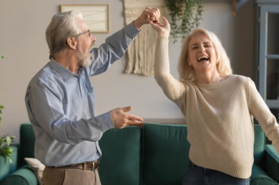 Senior couple is happy dancing in living room enjoying the freedom of renting after selling primary residence.