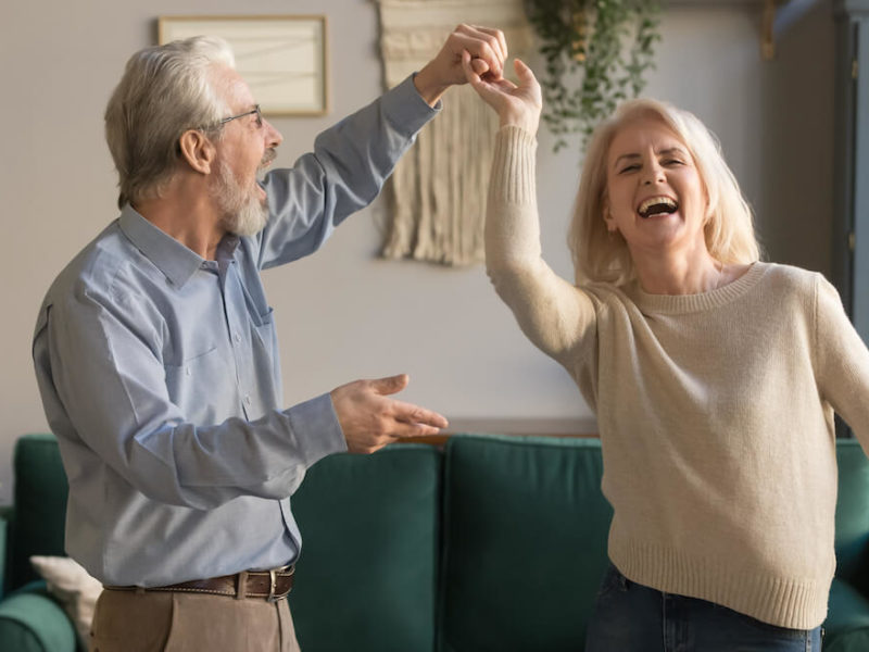 Senior couple is happy dancing in living room enjoying the freedom of renting after selling primary residence.