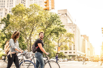 Young couple walking in big city street with bicycles enjoying city vs suburbs