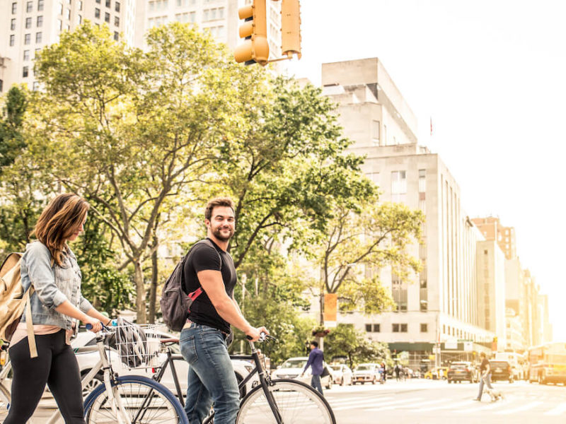 Young couple walking in big city street with bicycles enjoying city vs suburbs