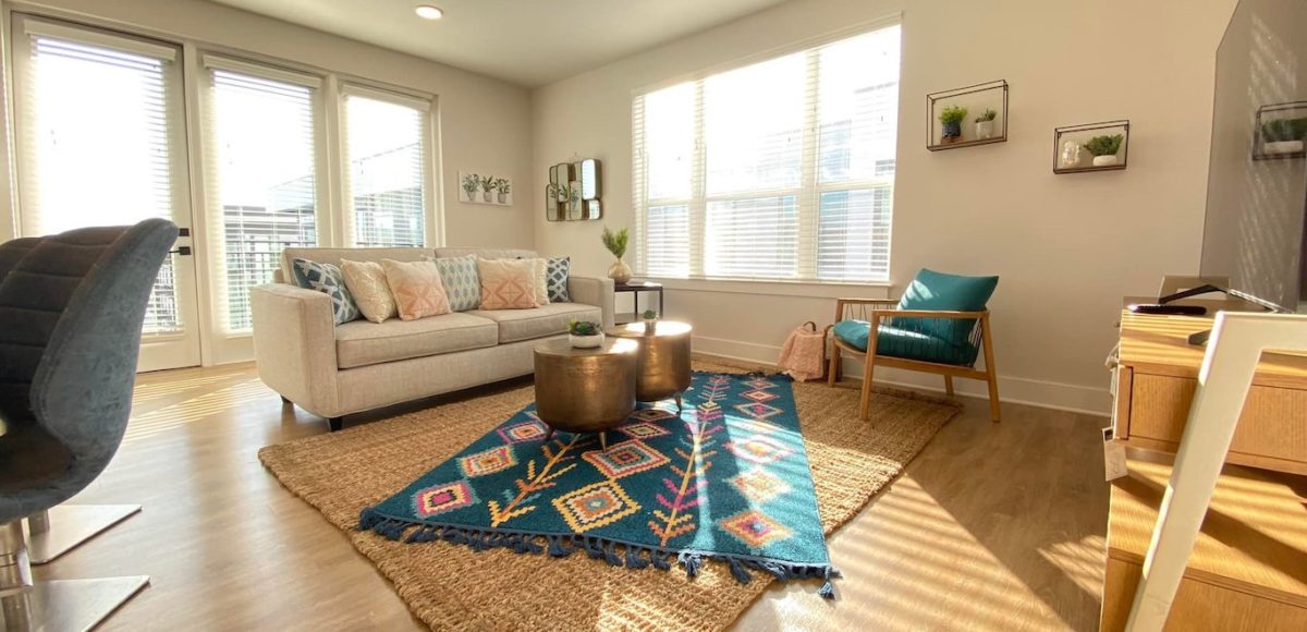Bright and well decorated 600 sq ft apartment with layered rugs, metallic accents, and arm chair provided by furniture rental near me.