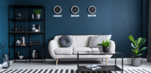 Dark blue moody interior design example with white couch, black furniture, black and white rug, and dark blue walls