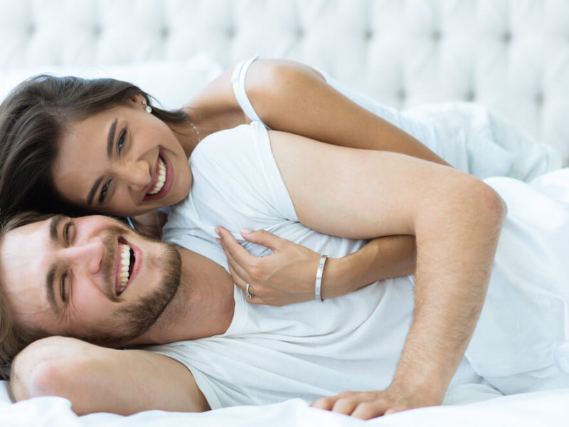 Young couple in stylish small bedroom cuddling on bed in white backround and clothing.