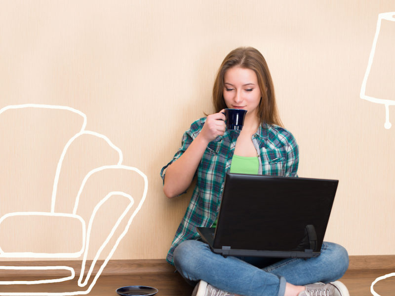 Young girl in empty apartment on laptop with legs crossed imaging furniture in her apartment wondering about fully furnished apartment rentals.