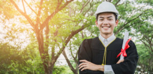 Engineering graduated students holding a diploma and wearing a helmet, smiling happily.