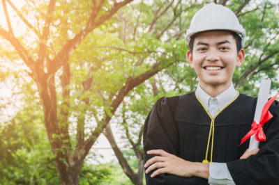 Engineering graduated students holding a diploma and wearing a helmet, smiling happily.