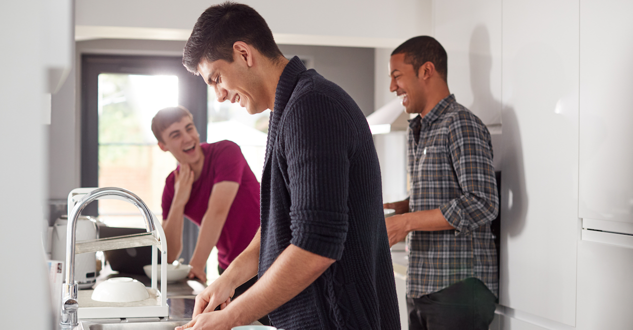 Group Of Male College Students In Shared House Kitchen Washing Up And Hanging Out Together