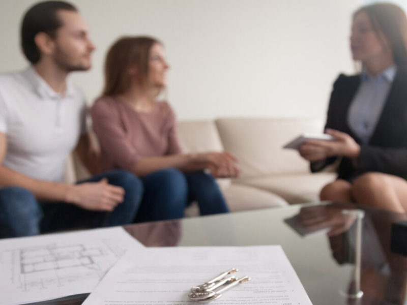 Young renters couple sitting on couch discussing renting apartment with real estate agent