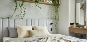 Stylish bedroom interior in modern apartment with small bed, wooden chest, home garden, white bedding, pillows and blanket. Sunny space with grey walls and brown wooden parquet. Template