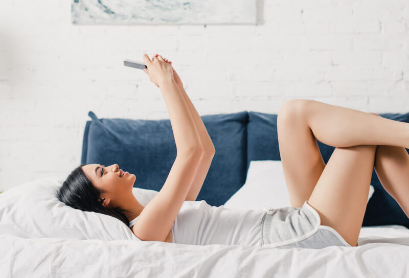 Smiling woman laying on bed looking at her phone