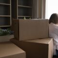 Woman facing window with boxes stacked behind her moving out after breaking up and learning how to move on from a long term relationship