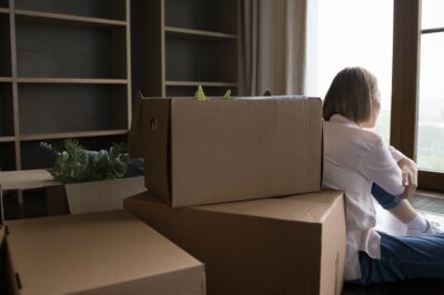 Woman facing window with boxes stacked behind her moving out after breaking up and learning how to move on from a long term relationship