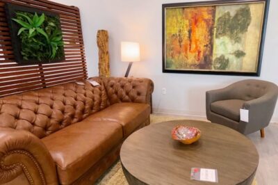 A brown leather couch with a colorful painting behind it