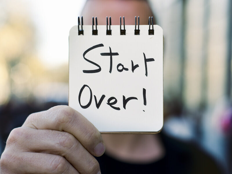 Man holding up a sign that says "start over!"