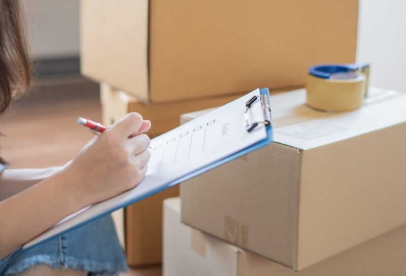 A woman checking items off her relocation checklist in front of a pile of boxes.