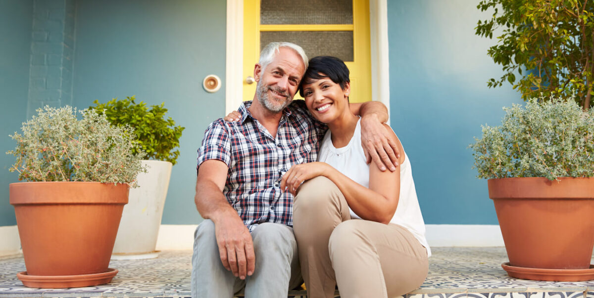 A smiling middle-age couple sitting on the front steps of their home.