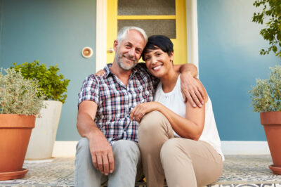 A smiling middle-age couple sitting on the front steps of their home.