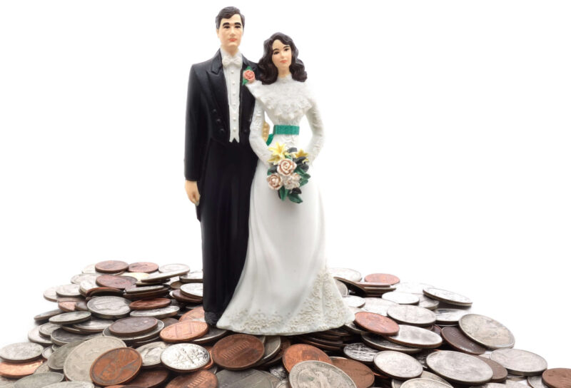 A plastic wedding topper figurine sits on a pile of coins.