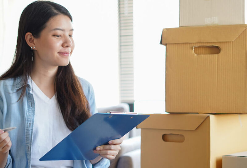 A young woman with a clipboard and moving boxes checking items off her checklist.