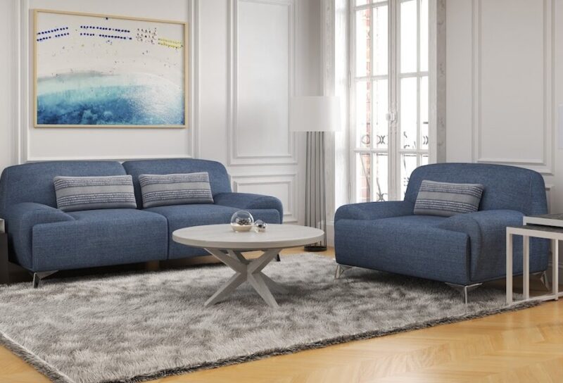 A bright, sunny living room with white, wood panel walls and blue sofa and chair.