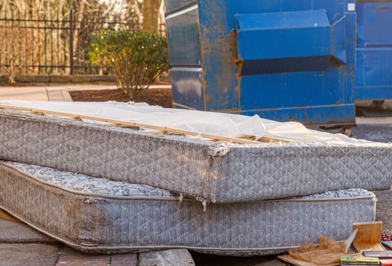 Mattresses left outside of apartment building after someone didnt know can you leave furniture in an apartment when you move out. Old mattresses are on the floor as garbage by two large blue dumpsters.